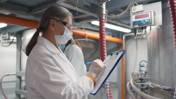 Portrait of Mature Woman in White Robe and Safety Mask Standing in Production Department 