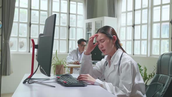 Young Asian Woman Doctor Is Using Computer And Headache In Workplace. Medical Concept