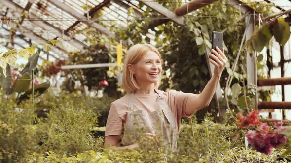 Female Farmer Talking on Video Call on Smartphone in Greenhouse