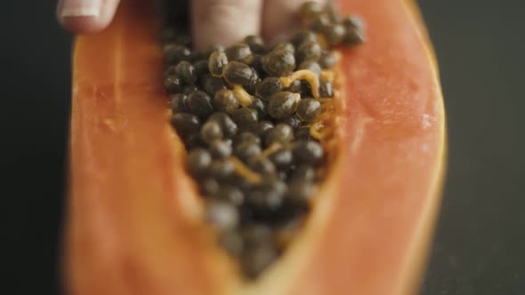 Close up of female fingers diving into the seeds of papaya cut in half