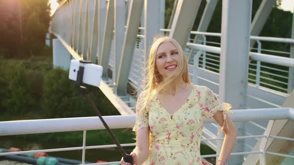 Woman Taking Selfie on Bridge. Cheerful Pretty Blonde Girl Standing on Pedestrian Bridge and Taking