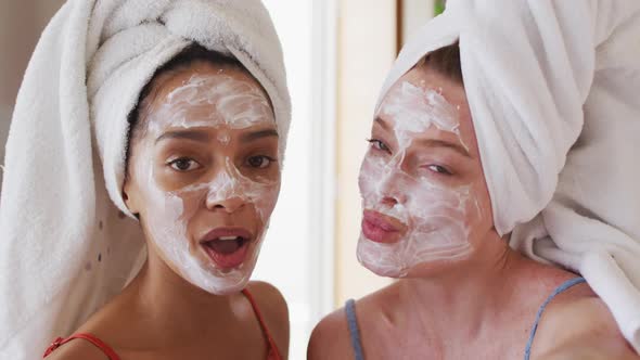 Diverse happy female friends wearing towels on heads and cleansing masks taking selfie at home