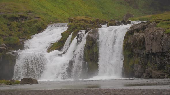 Landscape view of famous green Kirkjufell Mountain and Waterfall landmark with water , far near Grun