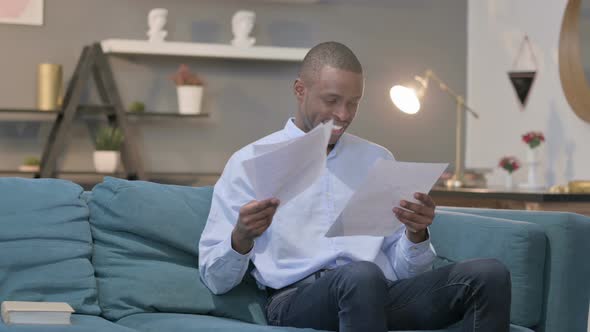 African Man Upset While Reading Documents on Sofa