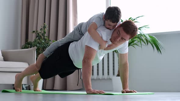 Happy Father Doing Push Up Exercise with Son on Back at Gym