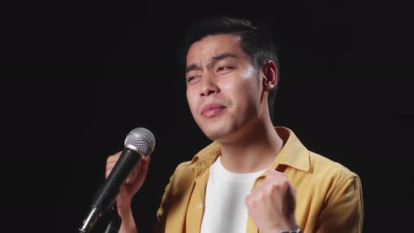 Side View Of Asian Man Singer Singing Into Microphone On Black Background