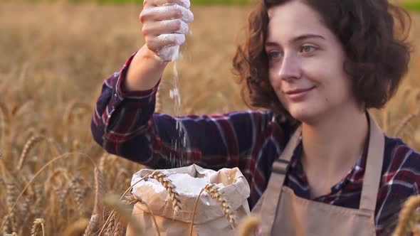 Smiling Woman In Apron Out Of Hand In Craft Bag With A Slide Of Flour. Concept For Preparation Flour