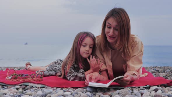 A Little Girl with Her Beautiful Mother Reading Book While Having Picnic By the Sea