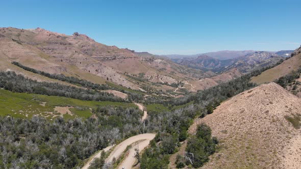 Aerial view of a winding dirt road through the mountains. Car can be seening. Droneing backwards.