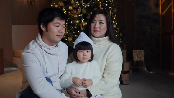 Korean Family with Daughter Sitting in White Sweaters Christmas Tree