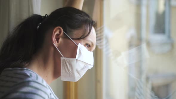 Concerned Sad Woman in Protective Medical Mask Looks Through Window Spbd