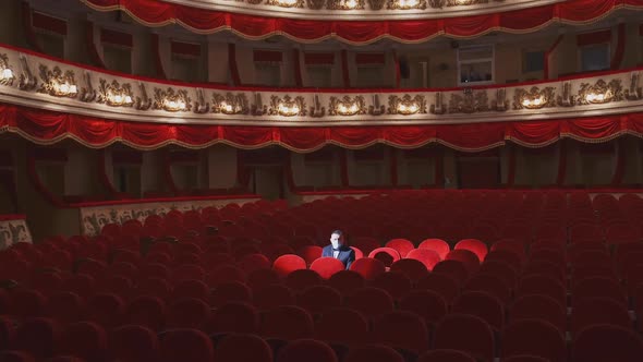 Rich man in mask in empty theater hall. Man spectator is sitting alone in large auditorium