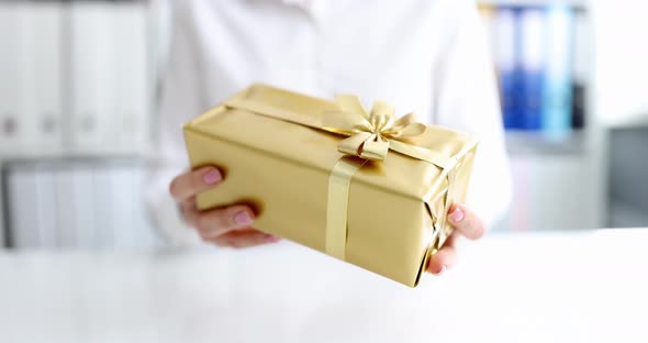 Person Gives Gift in Box with Golden Packaging and Bow