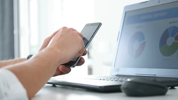 Businessman Using Smartphone And Checks Report Data On Laptop