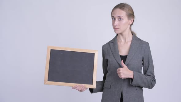 Happy Young Blonde Businesswoman Holding Blackboard and Giving Thumbs Up