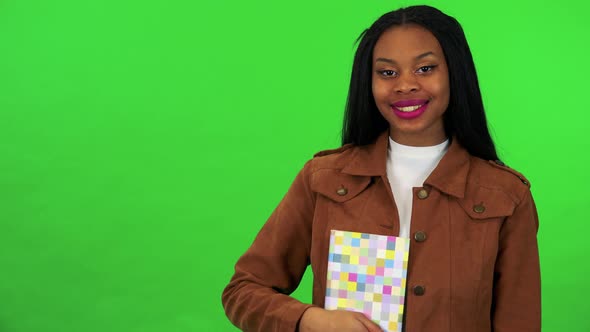 A Young Black Woman Holds a Book in Front of Her Chest and Smiles at the Camera - Green Screen