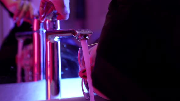 A Woman with Round Glasses Opens a Tap with Water and Drinks From It