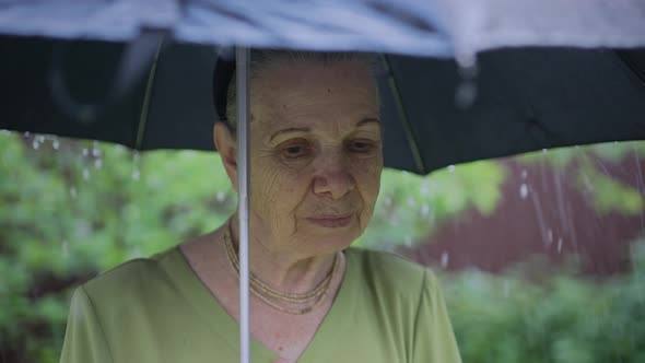 Sad Old Woman Under Umbrella at Rain