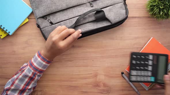 top view of young man putting office stationary in his bag 