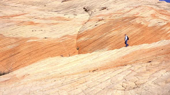 Panning view of woman hiking through color desert landscape layers