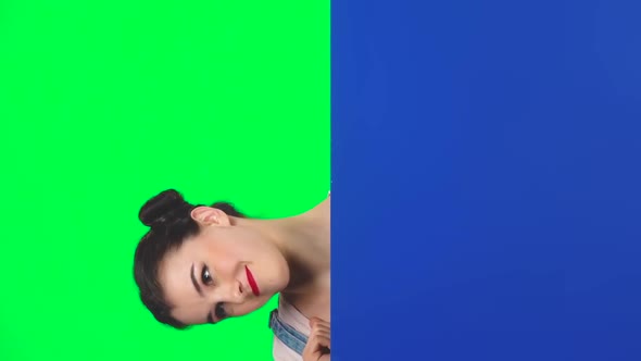 Girl Looking Out From Behind Blue Blank Placard on Green Screen at Studio, Slow Motion