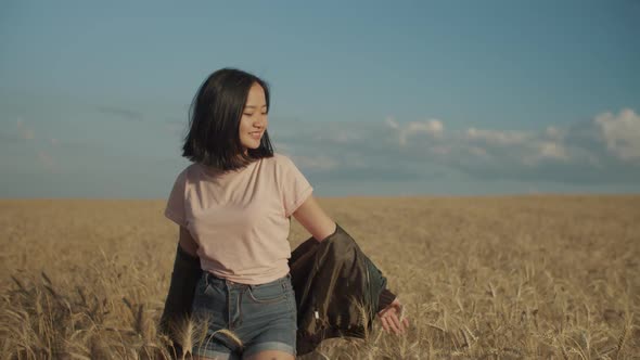 Joyful Asian Woman Walking in Wheat Field at Sunset