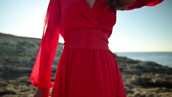 Closeup of a Woman in a Flattering Red Dress Walking on a Sea Rocky Landscape