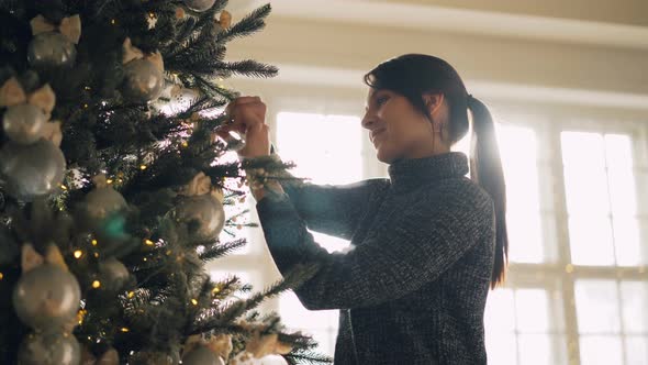 Smiling Student Is Decorating Artificial New Year Tree Hanging Silver Balls and Lights