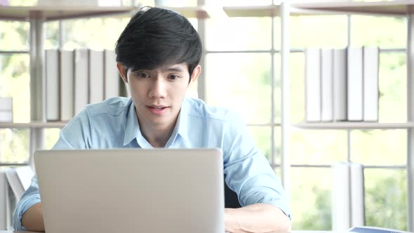 Young Asian business man working at home with laptop and papers on desk, working remotely