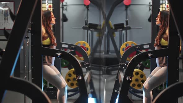 Beautiful girl in the gym is squatting with a barbell. Strength exercises for the feet.