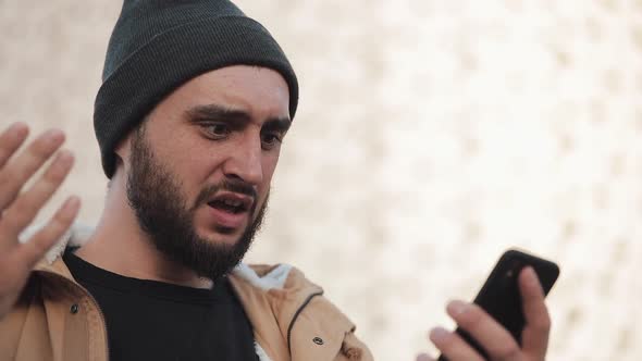 Young Man Reading Bad News on Smartphone Standing Near Office Center. He Looks Shockes and Worried