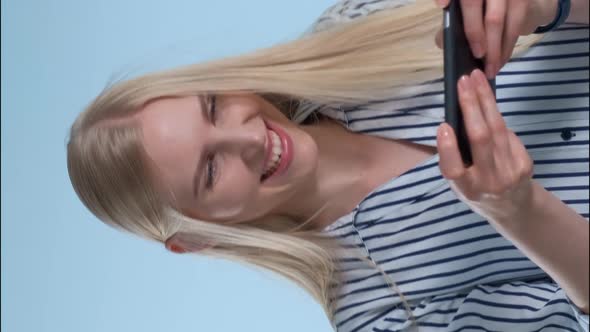Pretty Blonde Girl Playing Games on Smartphone on Blue Background