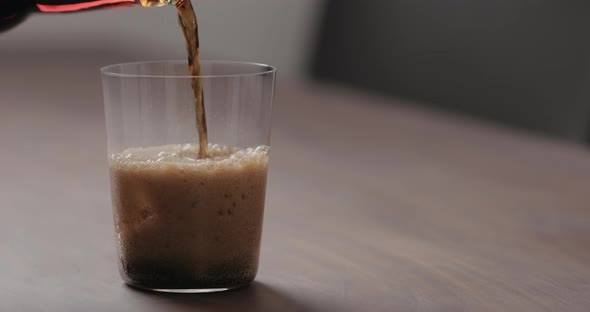 Slow Motion Pour Cola Into Tumbler Glass with Ice on Walnut Table with Copy Space