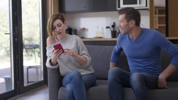 Man Entering Living Room Sitting Down on Couch As Woman Ignoring Partner Surfing Internet on