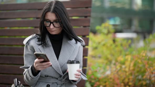 Businesswoman is Resting in Park in Autumn Day and Sending Message By Cell Phone