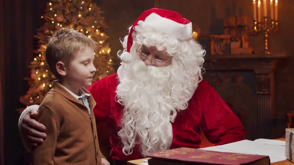 Santa Claus and little boy. Cheerful Santa is working at the table. Christmas concept.