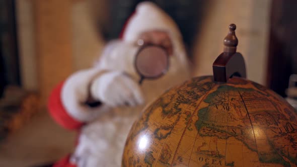 Santa Claus with globe. Big round globe and Santa looking at it through the magnifying glass.