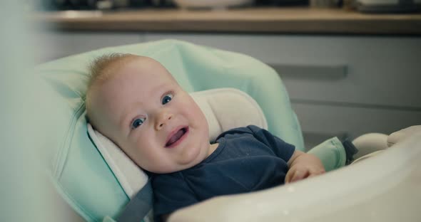 Cute Toddler in Kid Chair During Feeding with Spoon By Mother