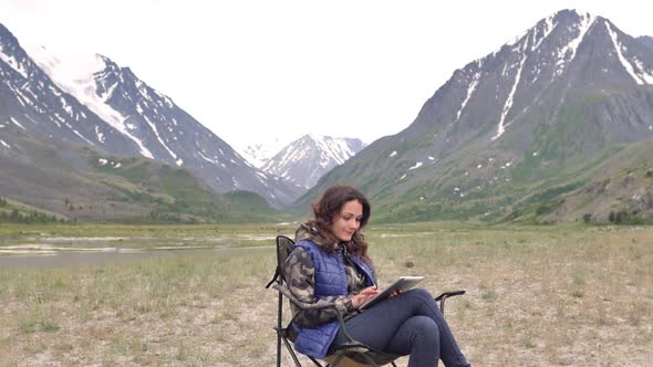 Woman Tourist with a Laptop, Prints, Works. Amid the Mountains Sitting on the Armchair