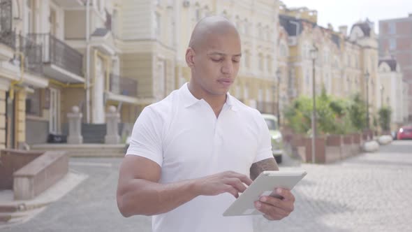 Portrait of Handsome Confident Bald Middle Eastern Man Typing on the Tablet Standing on the Street