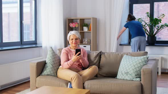 Old Woman with Smartphone and Housekeeper at Home