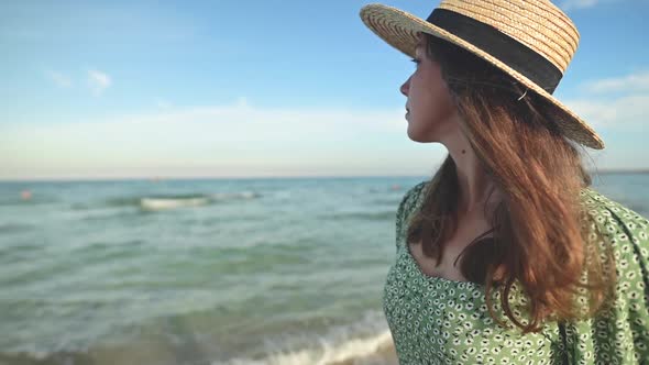 Romantic Portrait of Attractive Caucasian Young Woman in Green Dress and Straw Hat on the Seashore