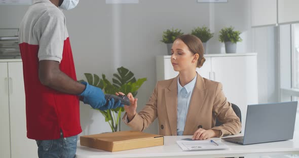 Deliveryman in Mask and Gloves Giving Pizza Box to Female Office Worker Paying with Credit Card