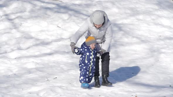 Kid Takes the First Steps in the Snow Walking with Mom