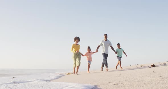 Smiling african american family walking and holding hands on sunny beach