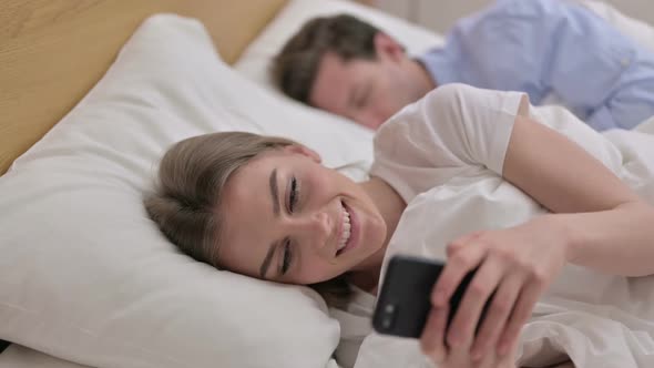 Cheerful Young Woman Using Smartphone in Bed