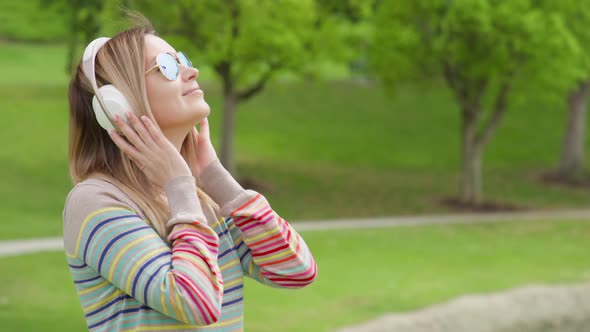 Young Woman Relaxing in Green Park on Summer Day in Wireless White Headphones 8K