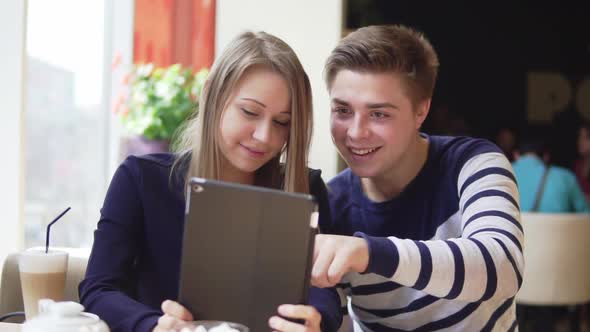 Young Attractive Couple Using Digital Tablet Computer Looking at the Screen in Cafe