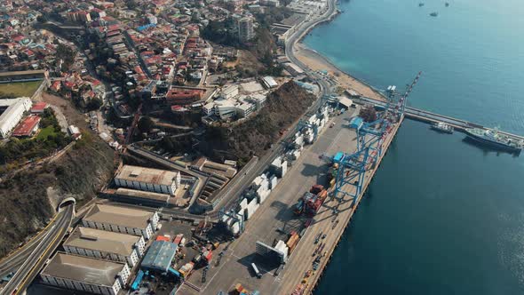 Aerial orbit of containers and cranes in Valparaiso Sea Port, Cerro Alegre hillside buildings in bac