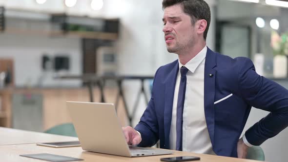 Hardworking Businessman with Laptop Having Back Pain in Office